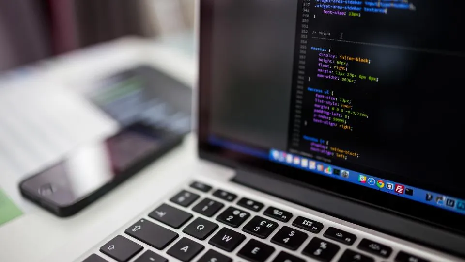 Close-up of a laptop screen showing colorful code, with a phone resting beside the keyboard