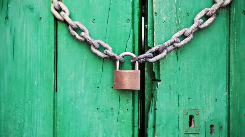 A padlock and chain locking two green wooden doors together